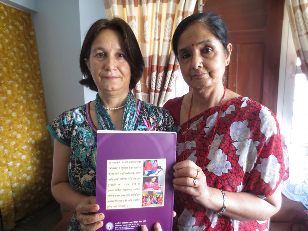 Two Nepali women stand holding a Hesperian book on women's health